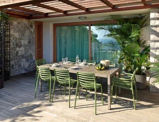 Gartentisch mit grünen Stühlen auf Holzterrasse unter Holzpergola mit Blick auf das Meer
