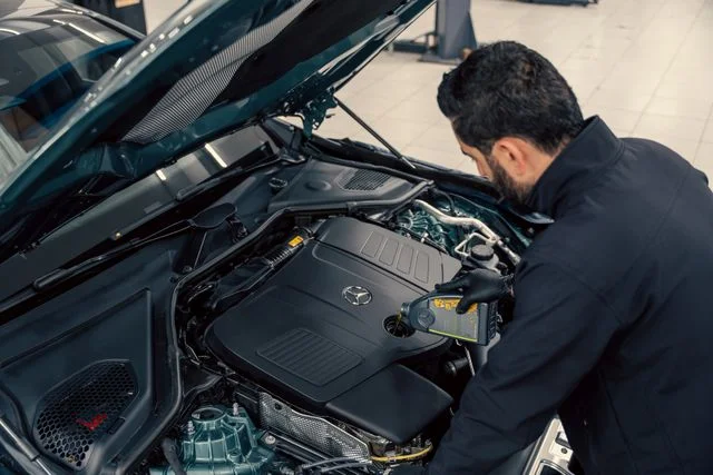 Ein Mechaniker prüft und füllt in einer Werkstatthalle Motoröl in ein Auto nach.