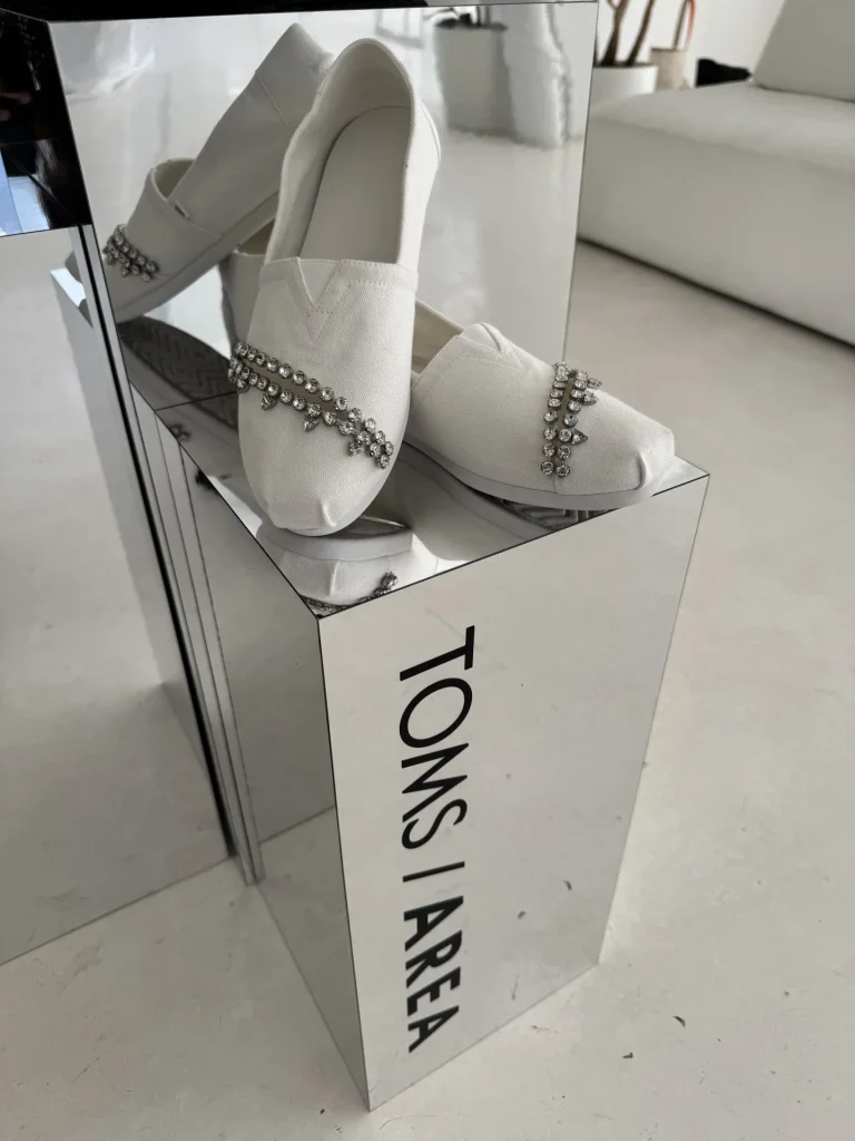 Weiße TOMS x AREA Alpargatas mit Crystal-Slit-Detail auf einer spiegelnden Oberfläche